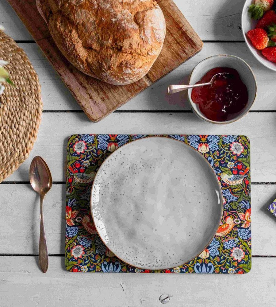 Table setting with a loaf of bread, bowl of jam, and floral placemat on a wooden table.