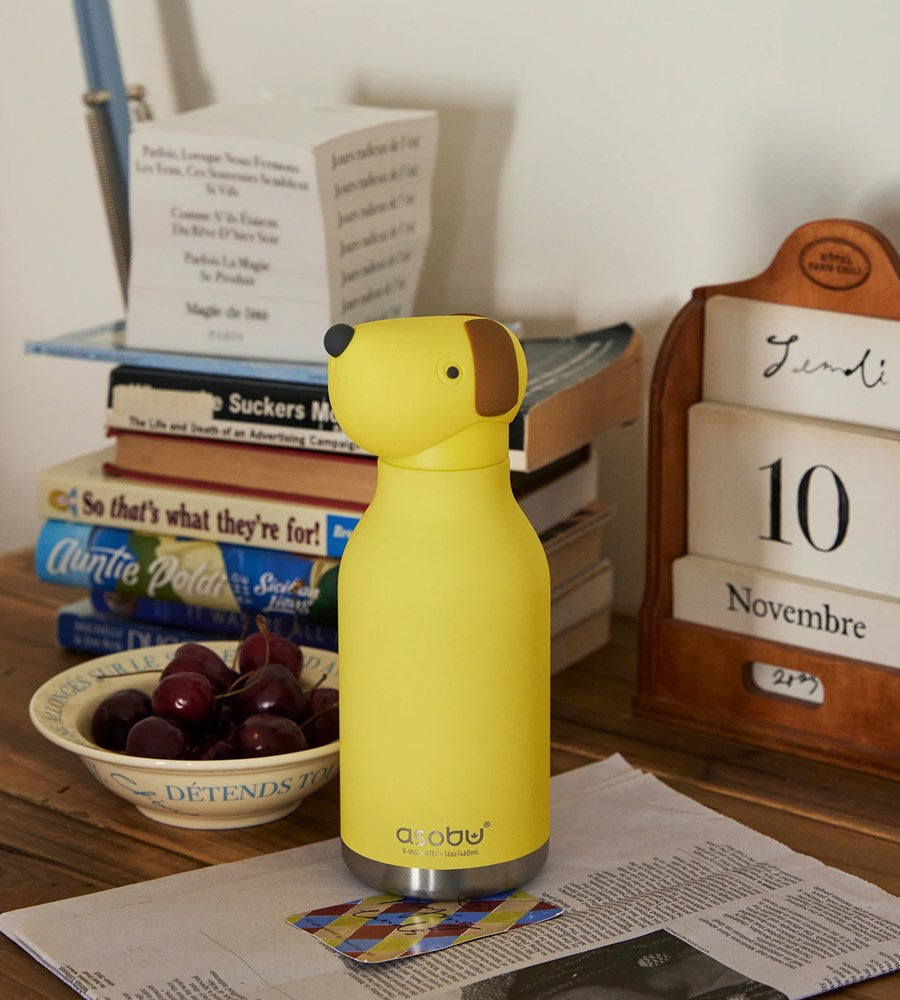 Yellow dog-shaped water bottle on a desk with books and a calendar in the background