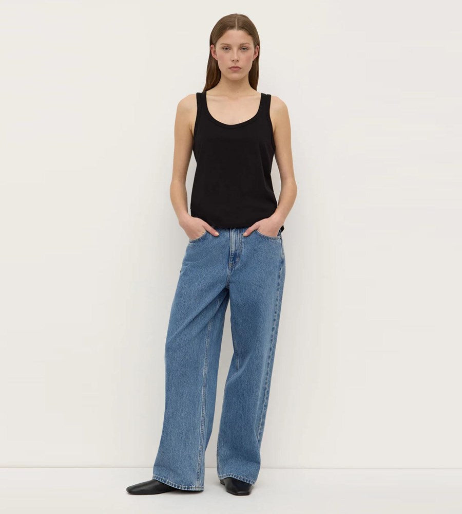 Person wearing a black tank top and blue jeans against a white background
