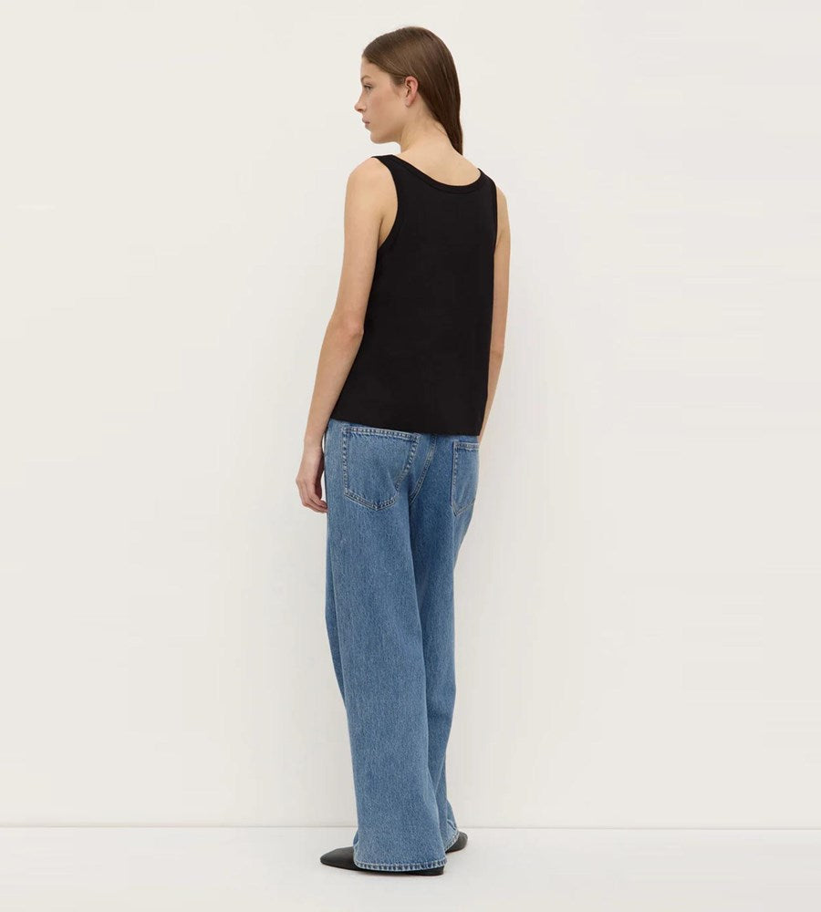 Person wearing a black sleeveless top and blue jeans against a white background