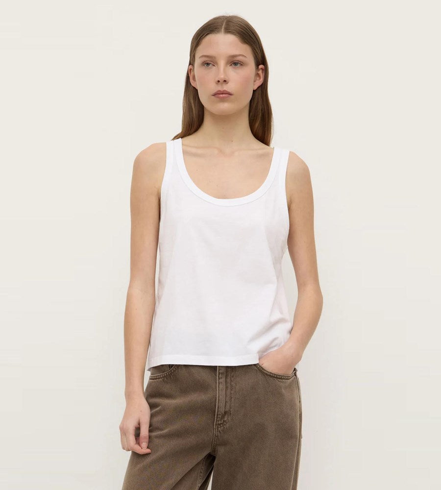 Woman wearing a white tank top and brown pants on a plain background