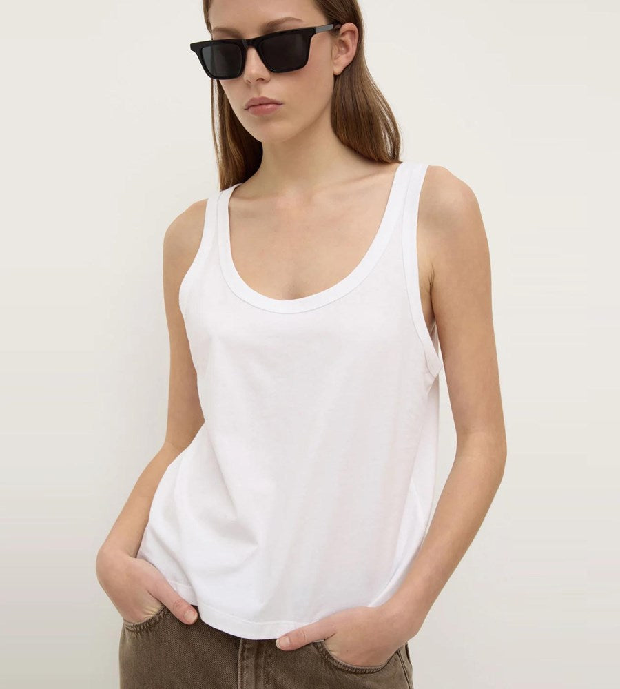 Person wearing a white tank top and sunglasses against a plain background
