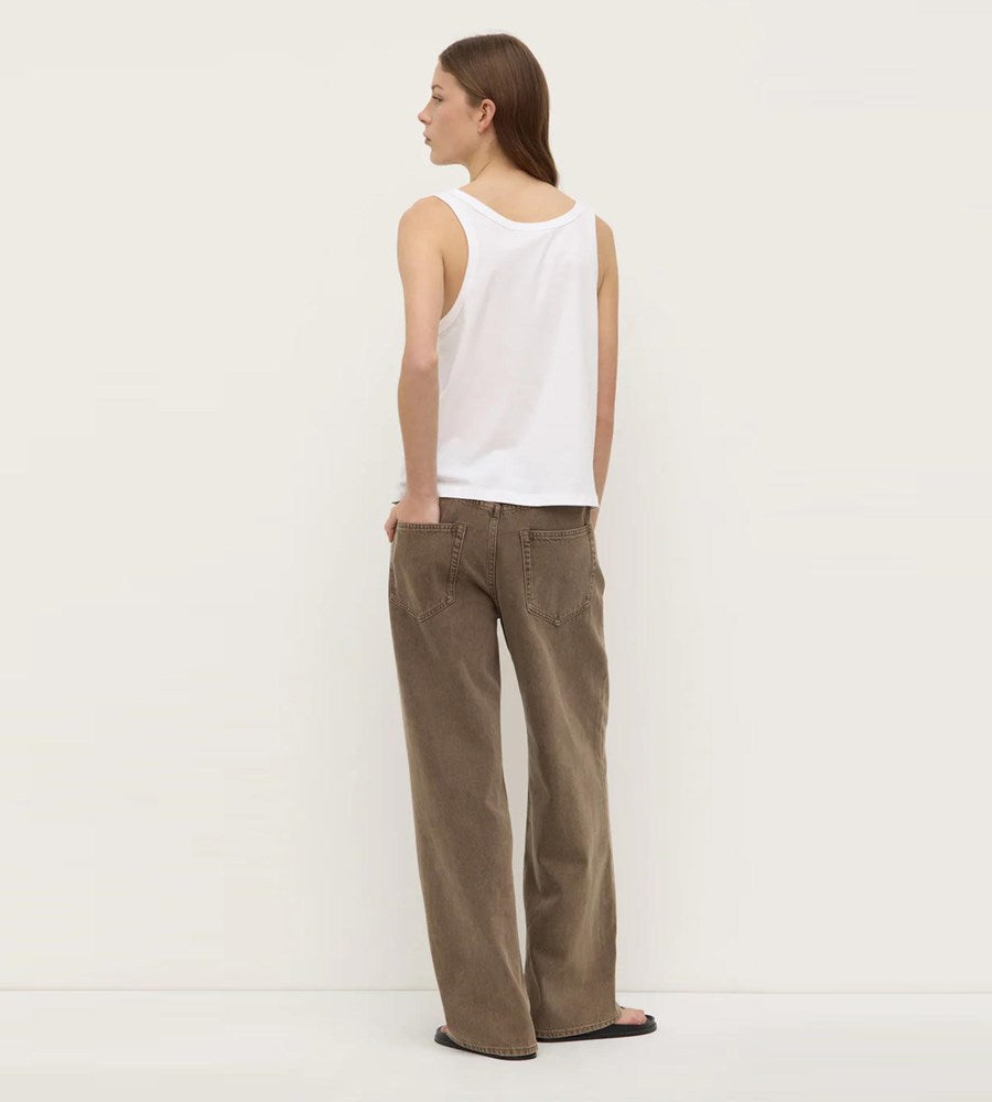 Woman wearing a white sleeveless top and brown pants against a plain background