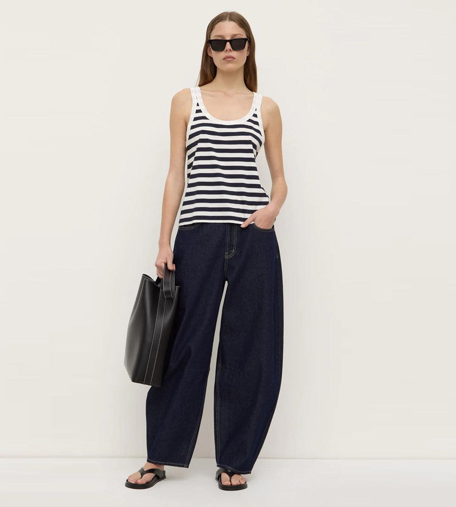 Woman wearing a black and white striped tank top and navy wide-leg pants, holding a black bag on a white background.