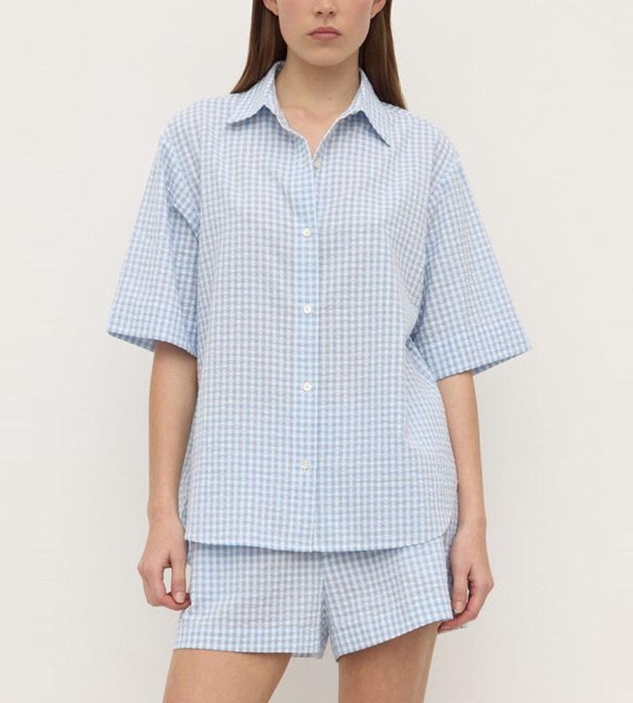 Person wearing a light blue checkered shirt and shorts set against a plain background