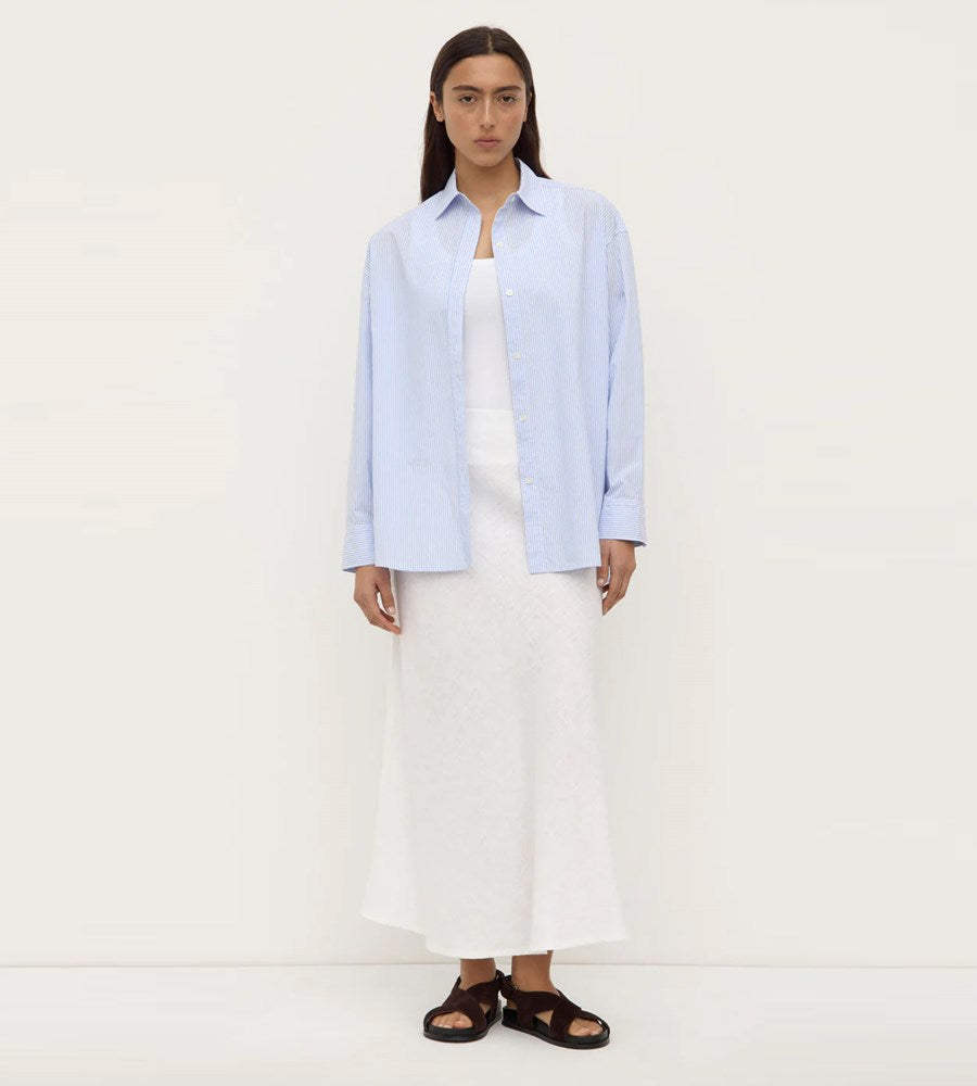 Person wearing a light blue shirt over a white dress on a plain background