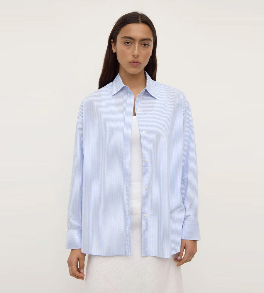 Person wearing a light blue striped shirt over a white top on a plain background