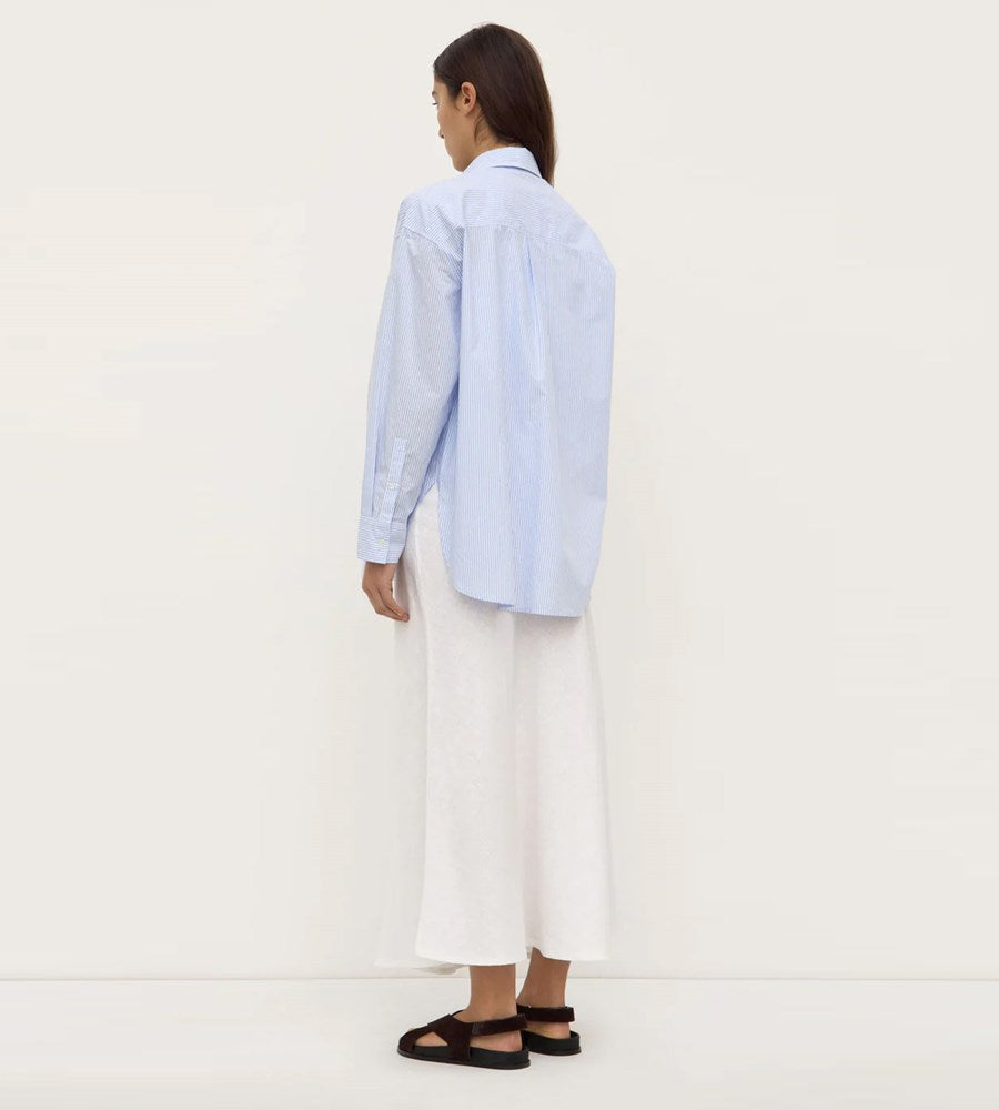 Person wearing a light blue striped shirt and white pants on a white background