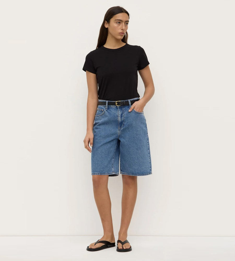 Person wearing a black t-shirt and blue denim shorts on a white background