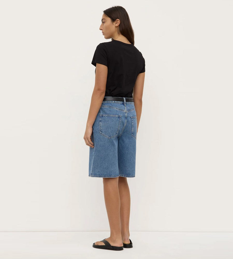 Person wearing blue denim shorts and a black t-shirt on a white background