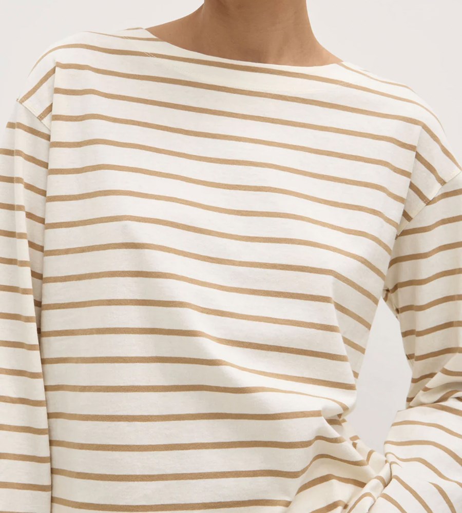 Close-up of a person wearing a white long-sleeve shirt with gold horizontal stripes on a plain background.