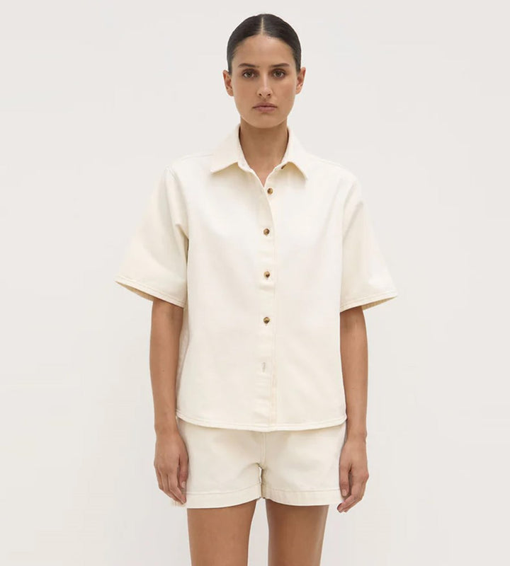 Woman wearing a cream-colored shirt and shorts set on a plain background