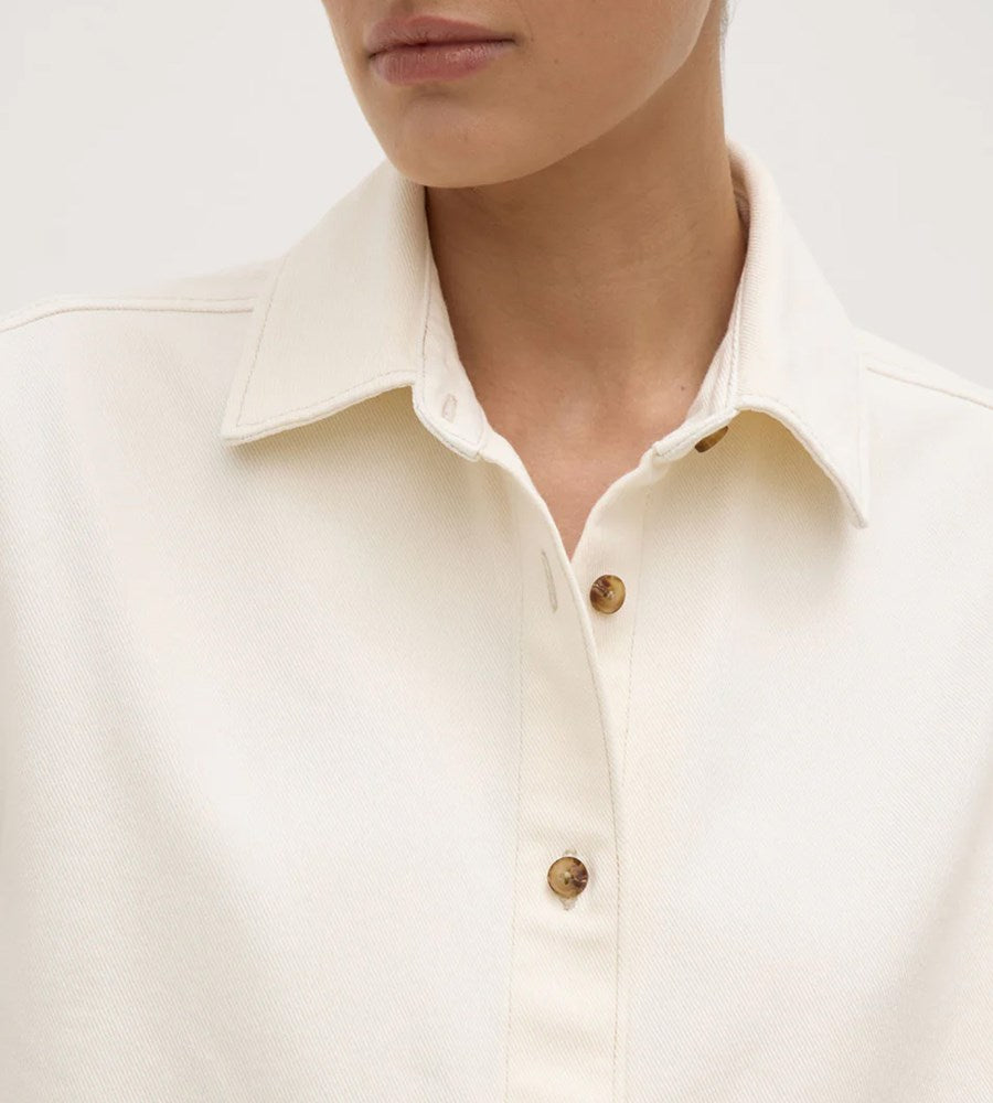 Close-up of a person wearing a cream-colored shirt with a collar and buttons.
