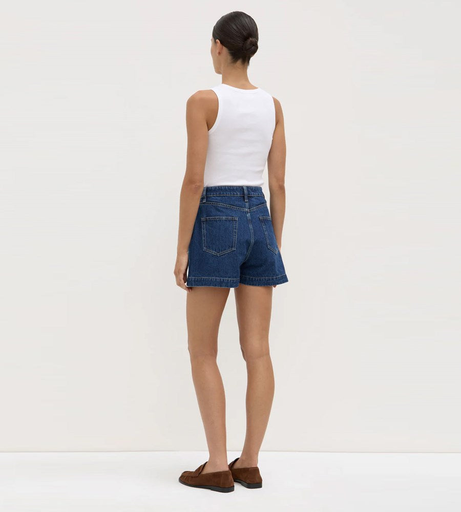Person wearing a white sleeveless top and blue denim shorts on a plain background