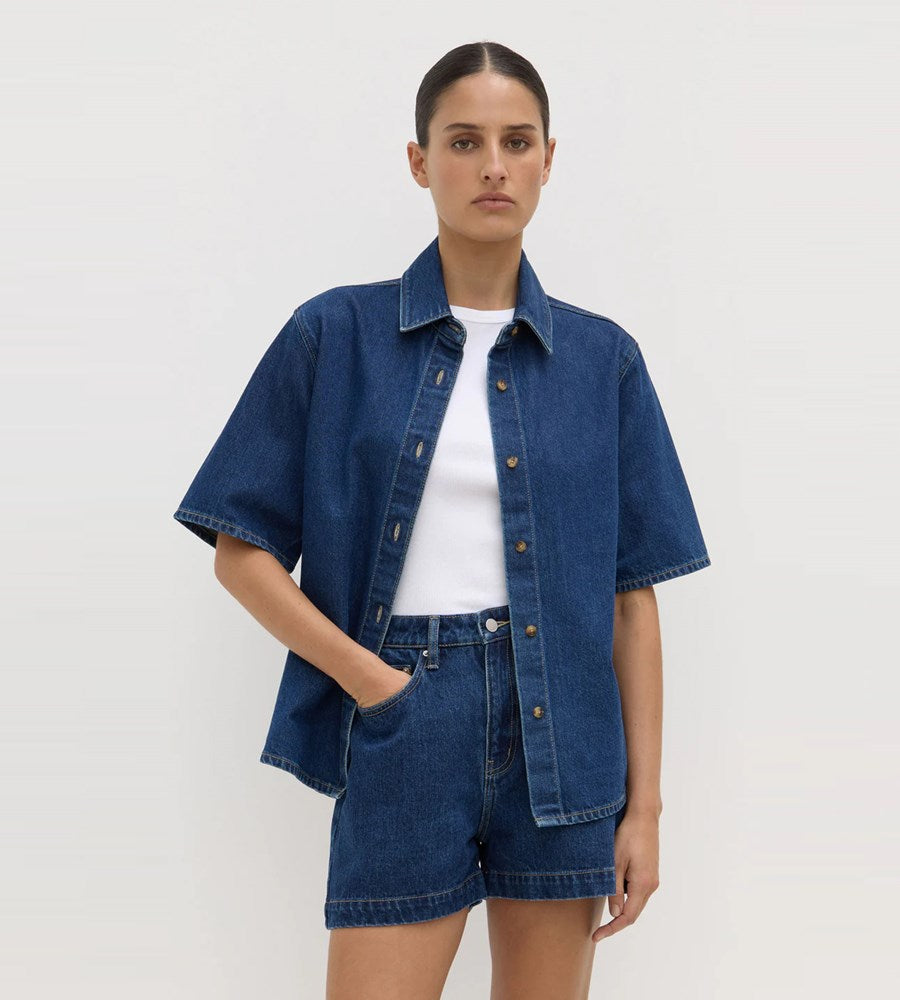Person wearing a denim jacket and shorts on a plain background