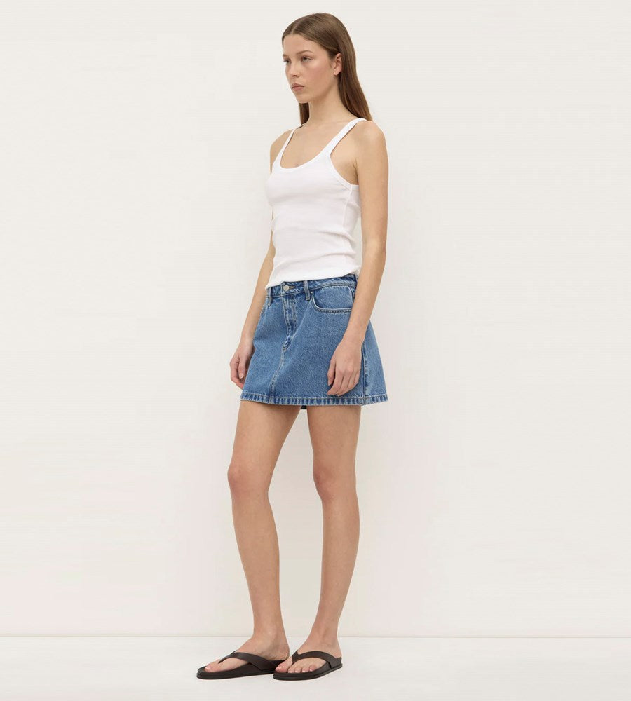 Woman wearing a white tank top and blue denim skirt on a plain background