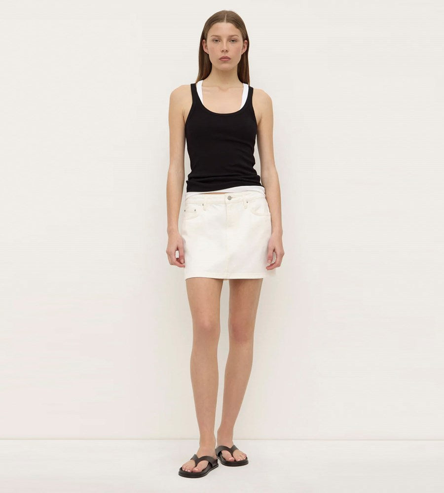 Woman wearing a black tank top and white skirt on a plain background