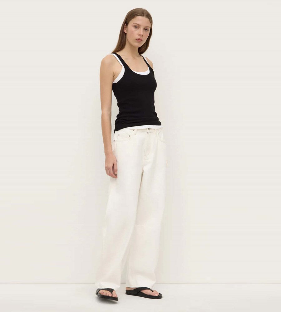 Woman wearing a black tank top and white pants on a plain background