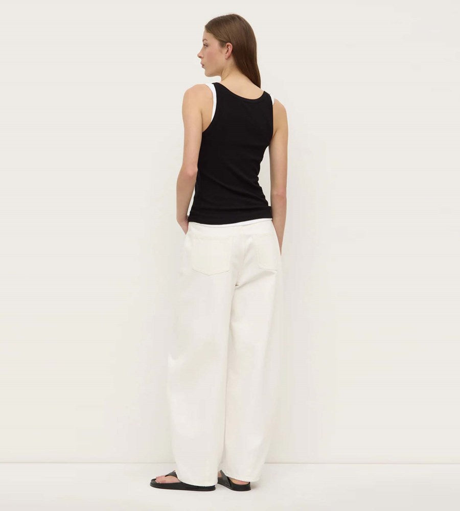 Woman wearing a black sleeveless top and white pants on a plain background