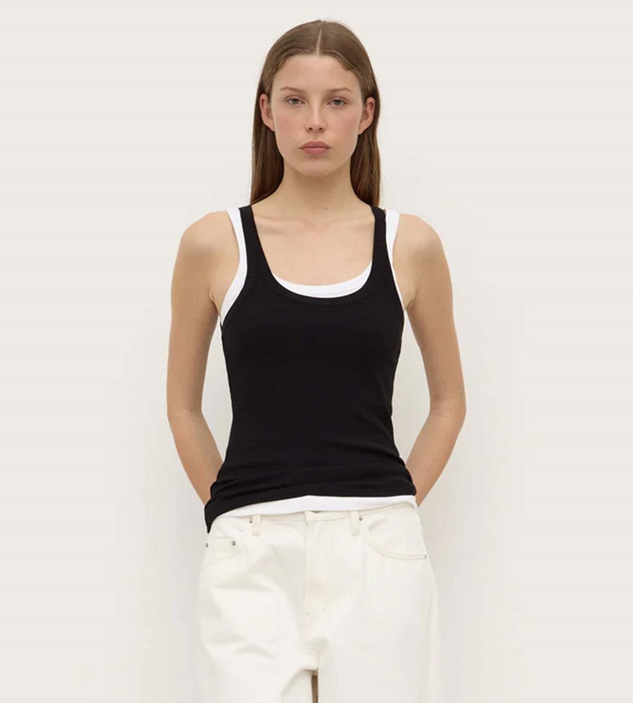 Woman wearing a black tank top with white trim against a plain background