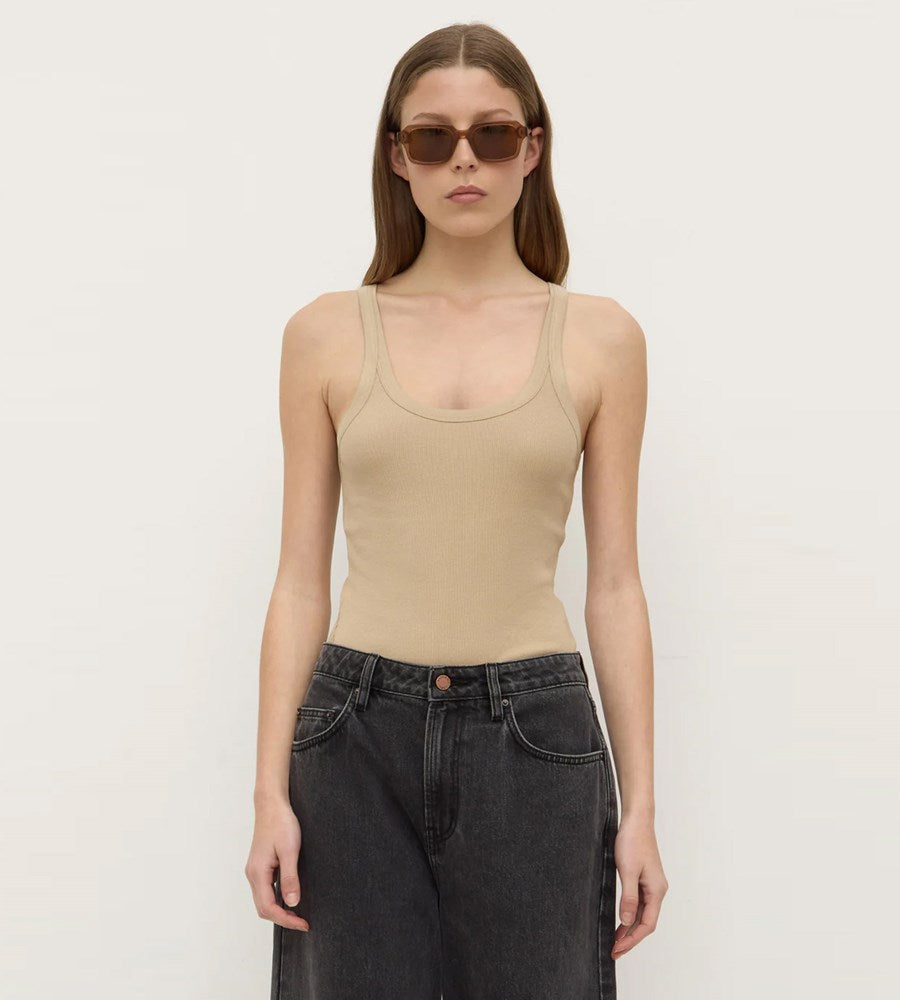 Woman wearing a beige tank top and black pants against a plain background