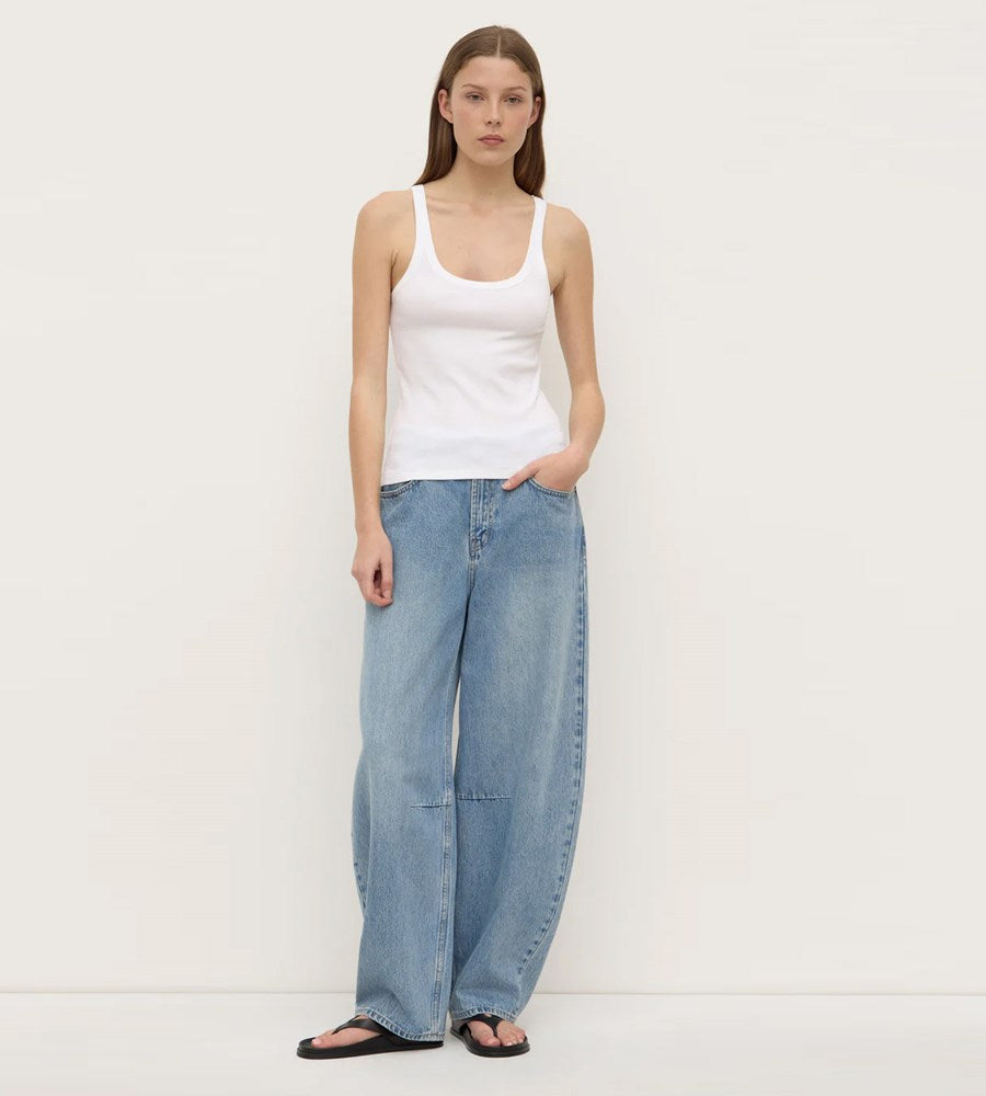 Woman wearing a white tank top and light blue jeans on a plain background