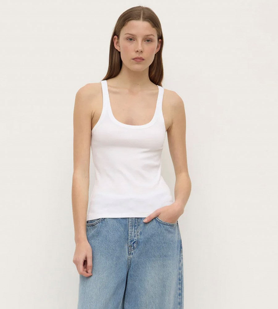 Woman wearing a white tank top and blue jeans against a plain background