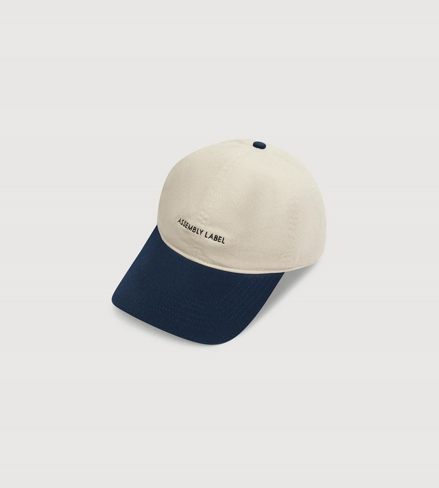 Two-tone cap with beige top and navy bottom on a light gray background