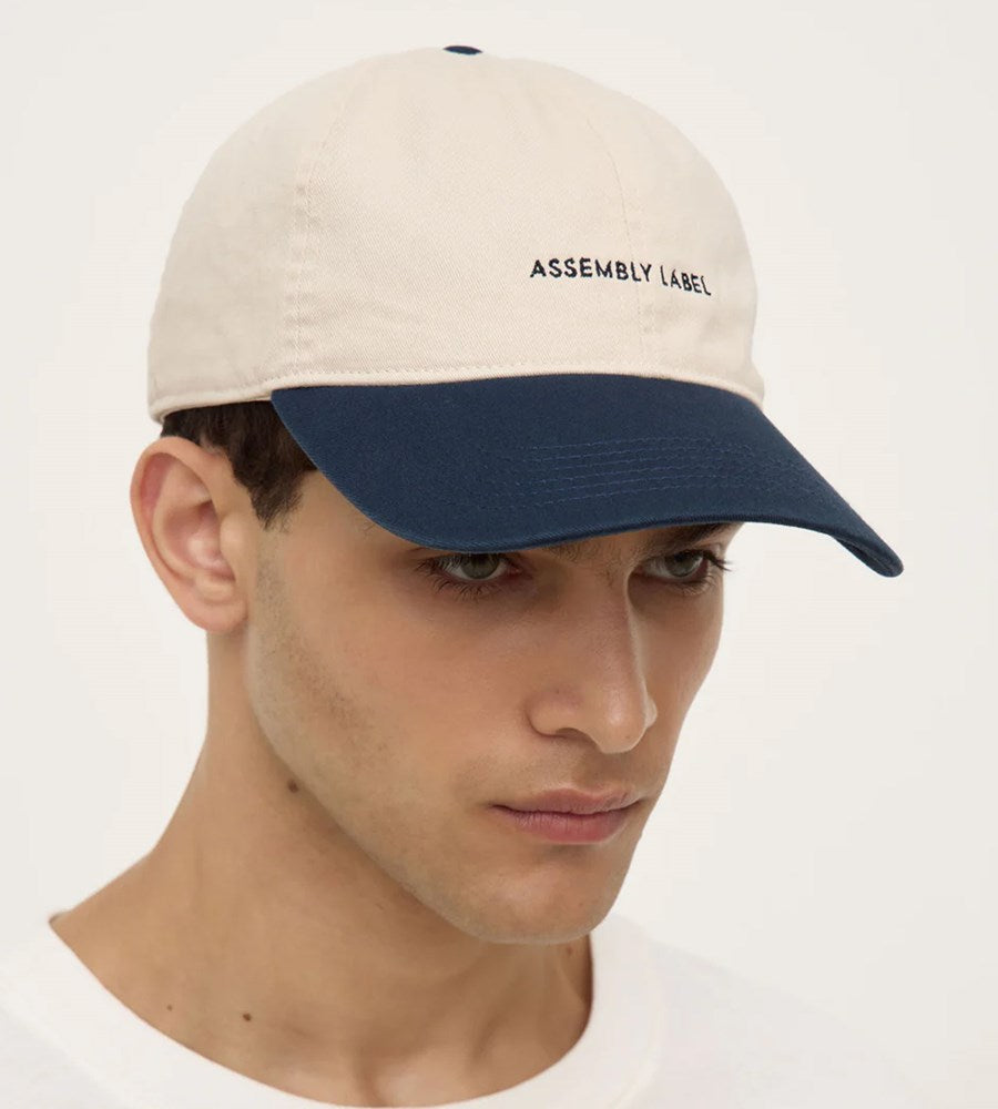 Man wearing a beige and navy cap with 'Assembly Label' on a white background