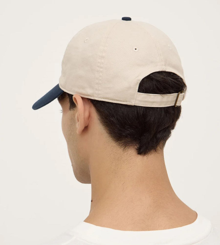 Beige cap with navy bill worn by a person on a white background