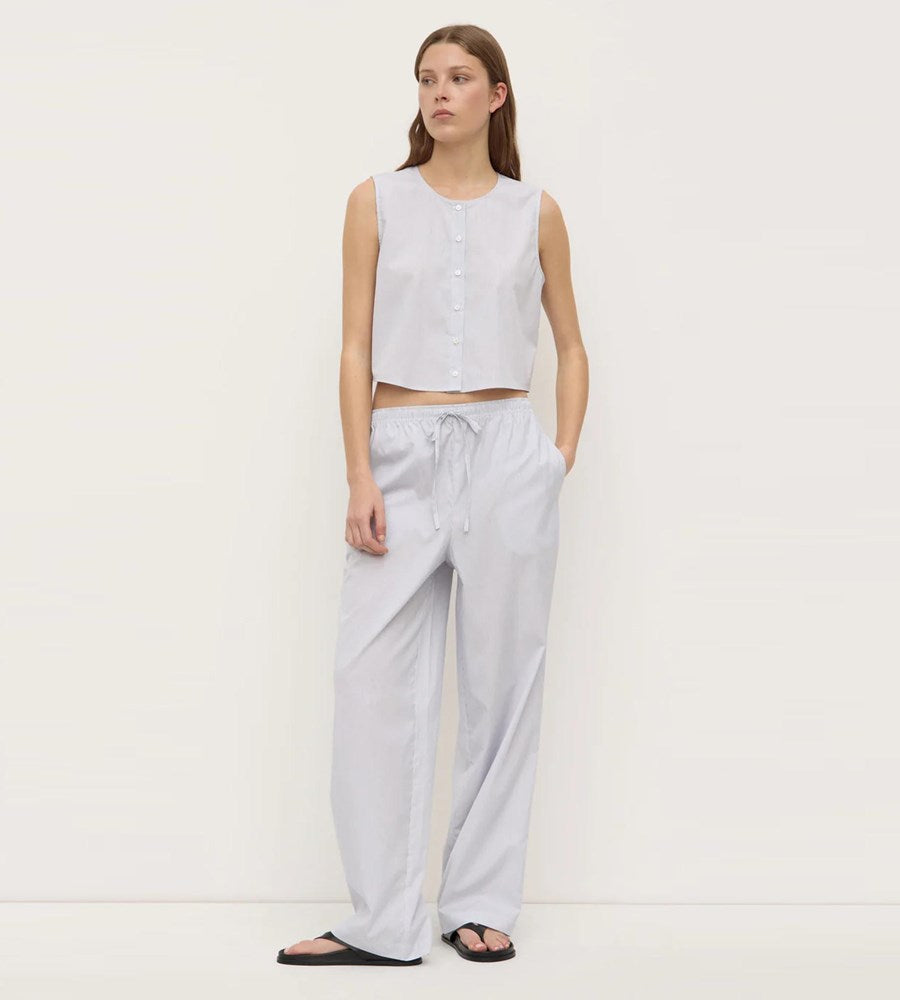 Woman wearing a sleeveless top and light gray pants on a white background