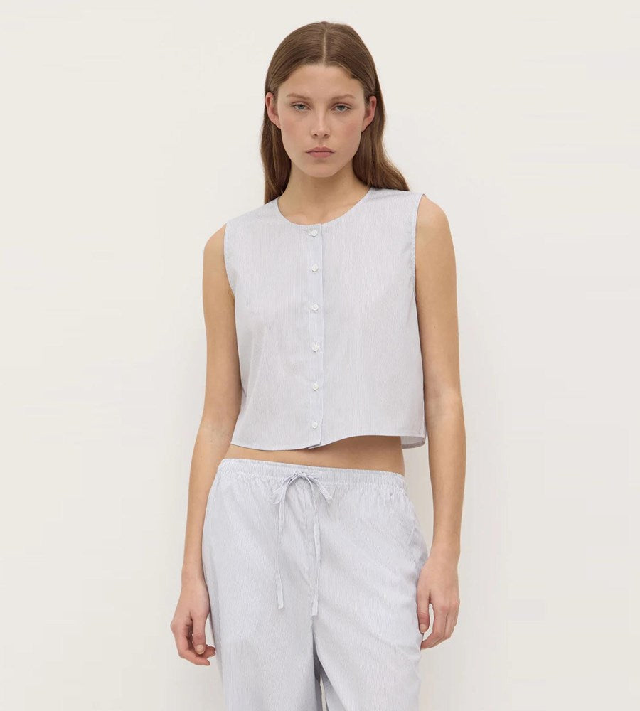Woman wearing a sleeveless white top and light gray pants on a plain background