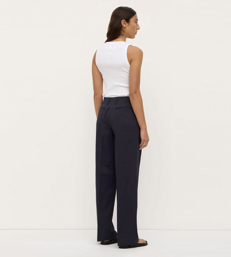 Woman wearing a white sleeveless top and dark pants against a white background