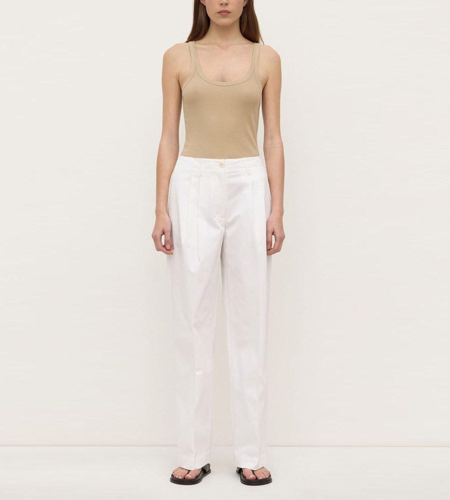 Person wearing a beige tank top and white pants on a plain background