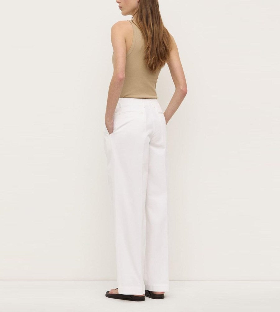 Woman wearing a beige tank top and white pants on a plain background