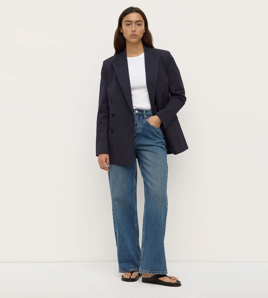Person wearing a navy blazer, white shirt, and blue jeans against a white background