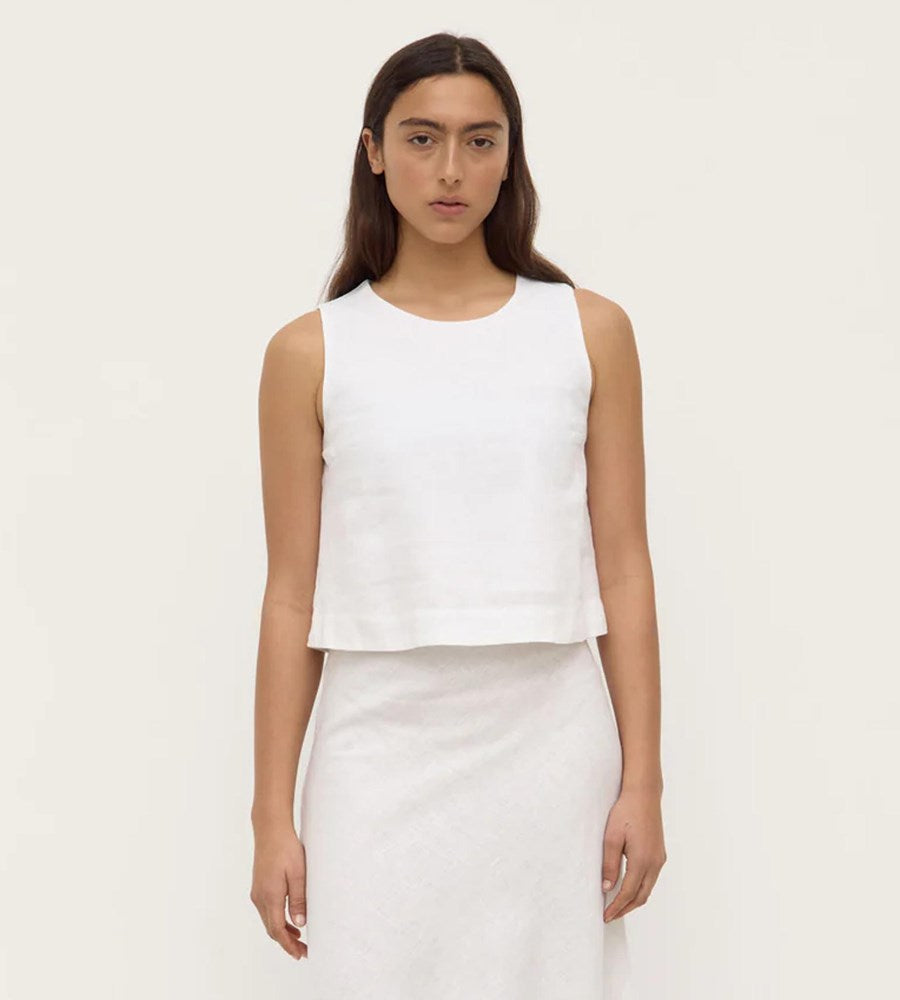 Woman wearing a white sleeveless top and skirt on a plain background