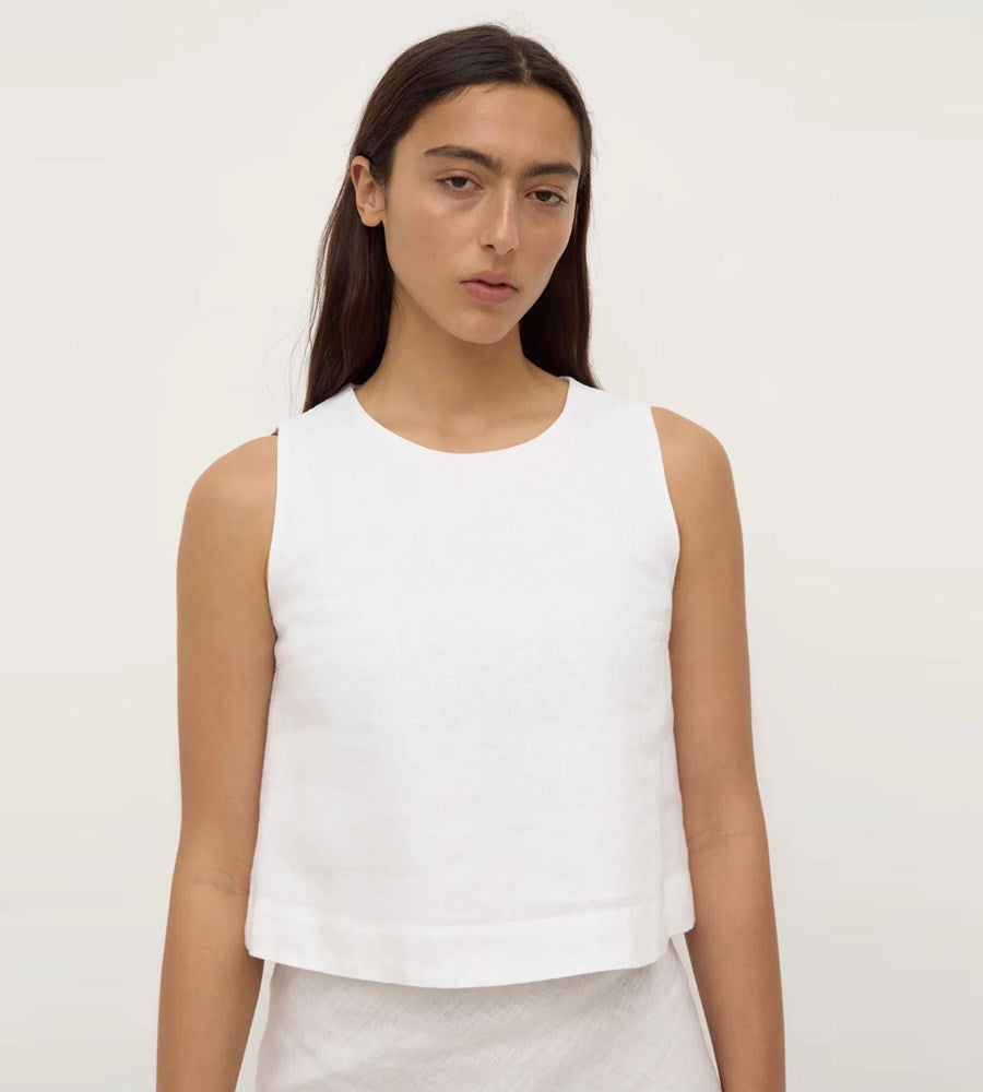 Woman wearing a white sleeveless top against a plain background