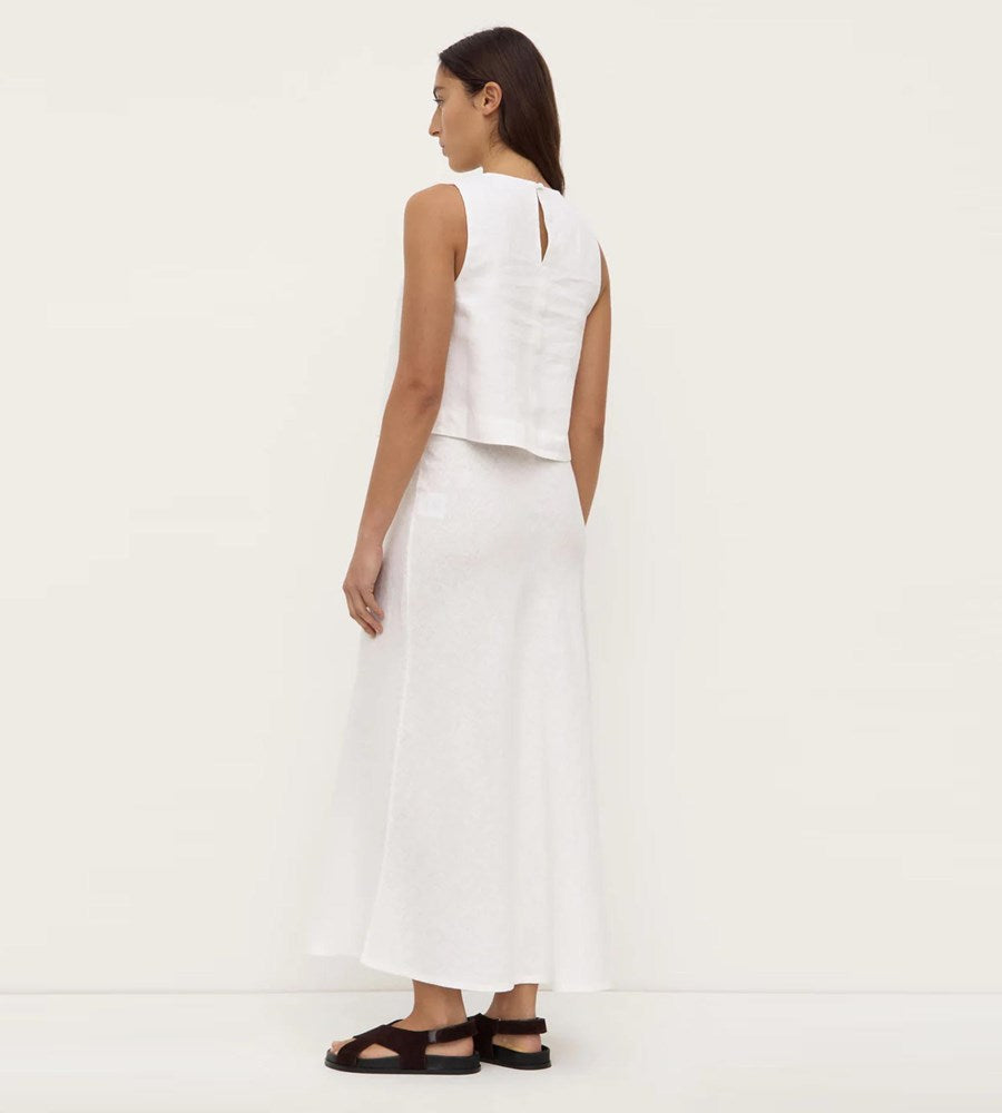 Woman wearing a white sleeveless top and white pants on a plain background