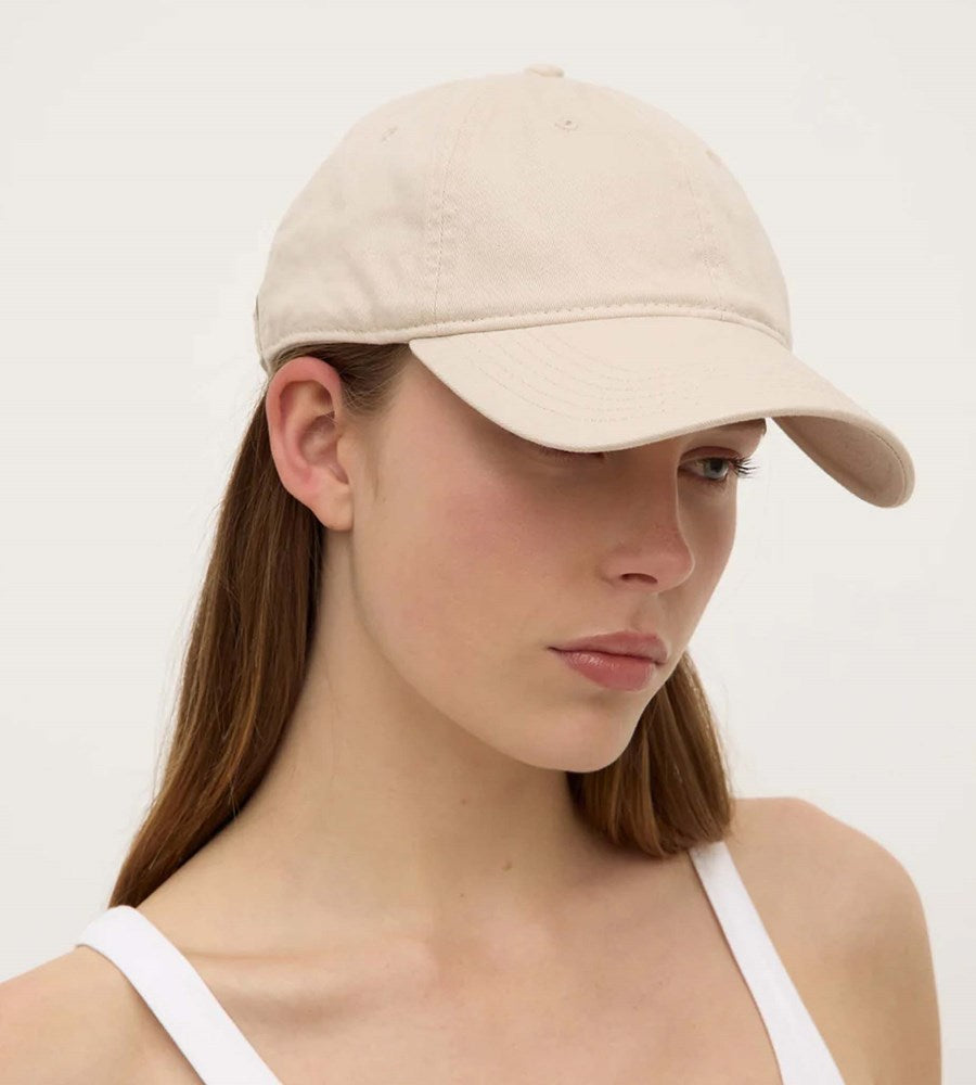 Woman wearing a beige baseball cap against a plain background