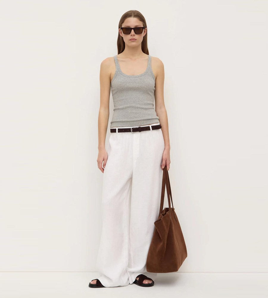 Woman wearing a gray tank top and white pants, holding a brown bag on a white background