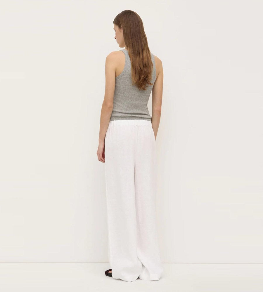 Woman wearing a gray sleeveless top and white pants on a plain background