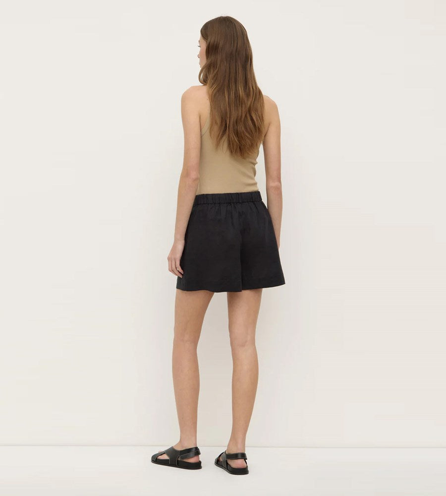 Woman wearing a beige top and black shorts against a white background