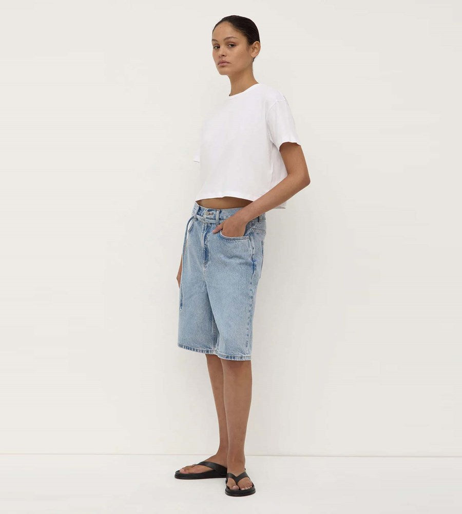 Person wearing a white crop top and light blue denim shorts on a plain background