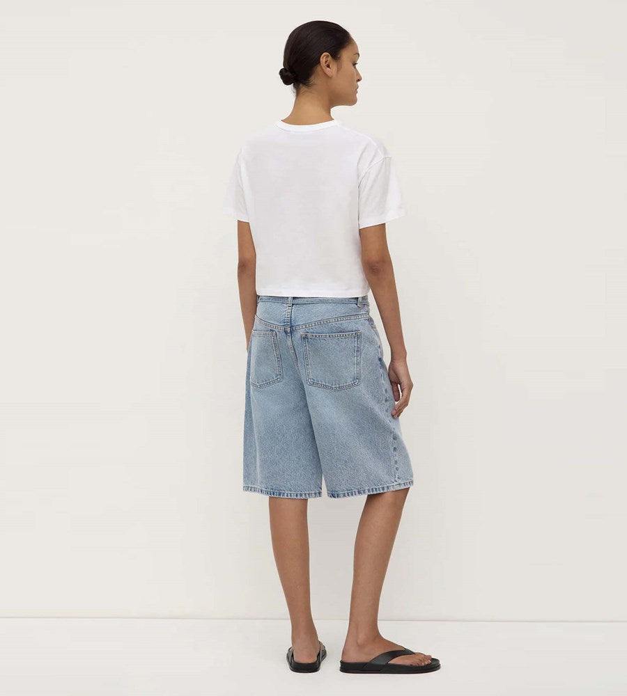 Person wearing a white t-shirt and light blue denim shorts on a plain background