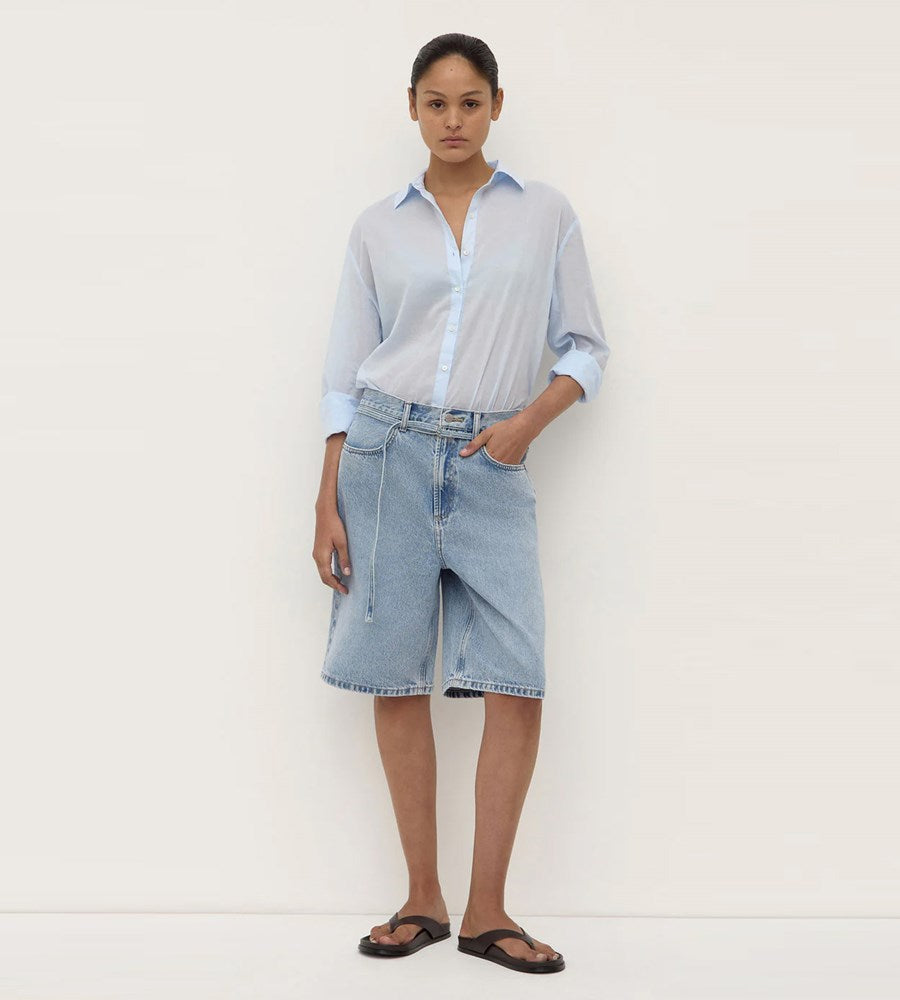 Woman wearing a light blue shirt and denim skirt against a white background