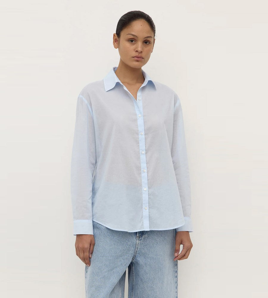 Woman wearing a light blue shirt and jeans against a plain background