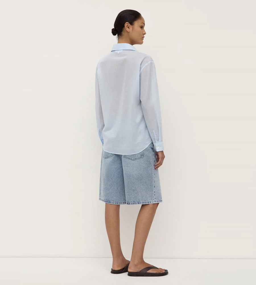 Woman wearing a light blue shirt and denim skirt on a white background