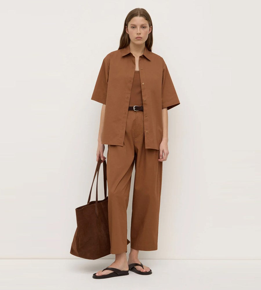 Woman wearing a brown outfit holding a matching bag against a white background