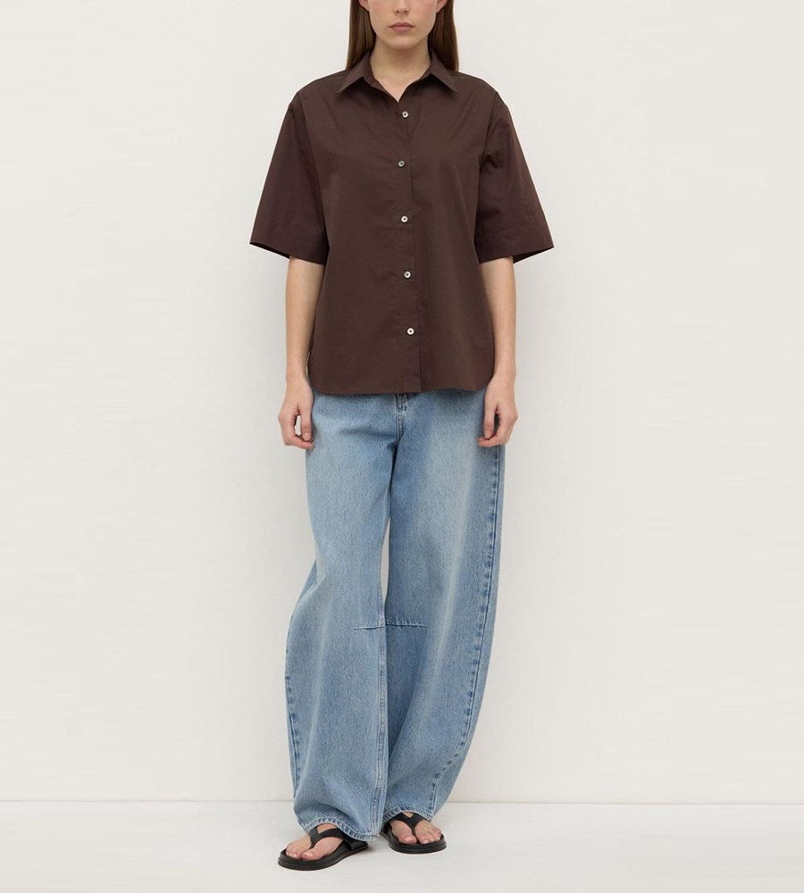 Person wearing a brown shirt and blue jeans against a white background